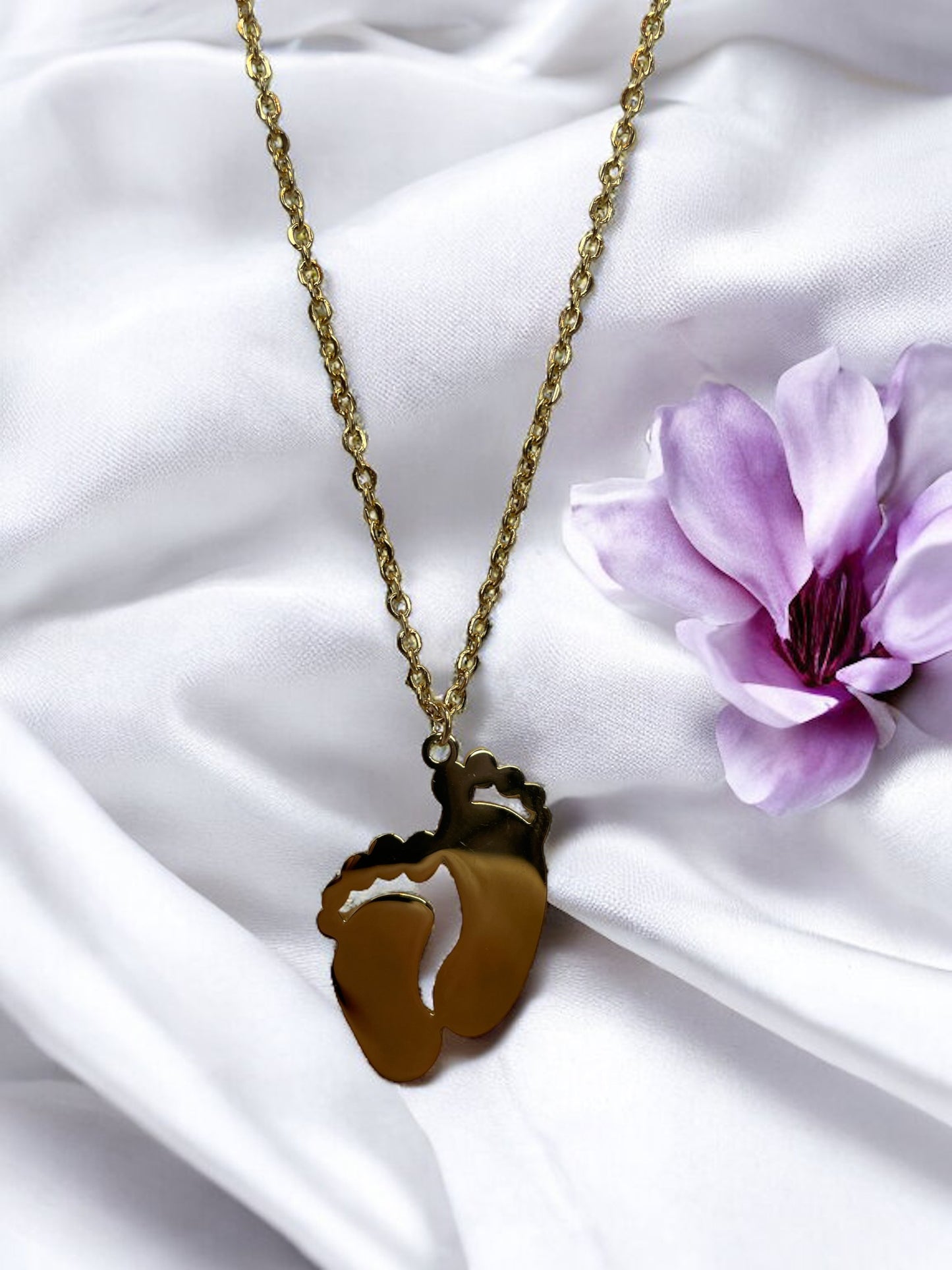 This image displays a charming necklace featuring a pendant shaped like a small child's footprint, signifying beginnings and growth. It has a polished finish with a choice between the classic sheen of stainless steel and the warm glow of gold plating. The pendant hangs gracefully on a matching chain, making it an ideal piece for everyday wear or as a sentimental gift to commemorate life's precious moments."