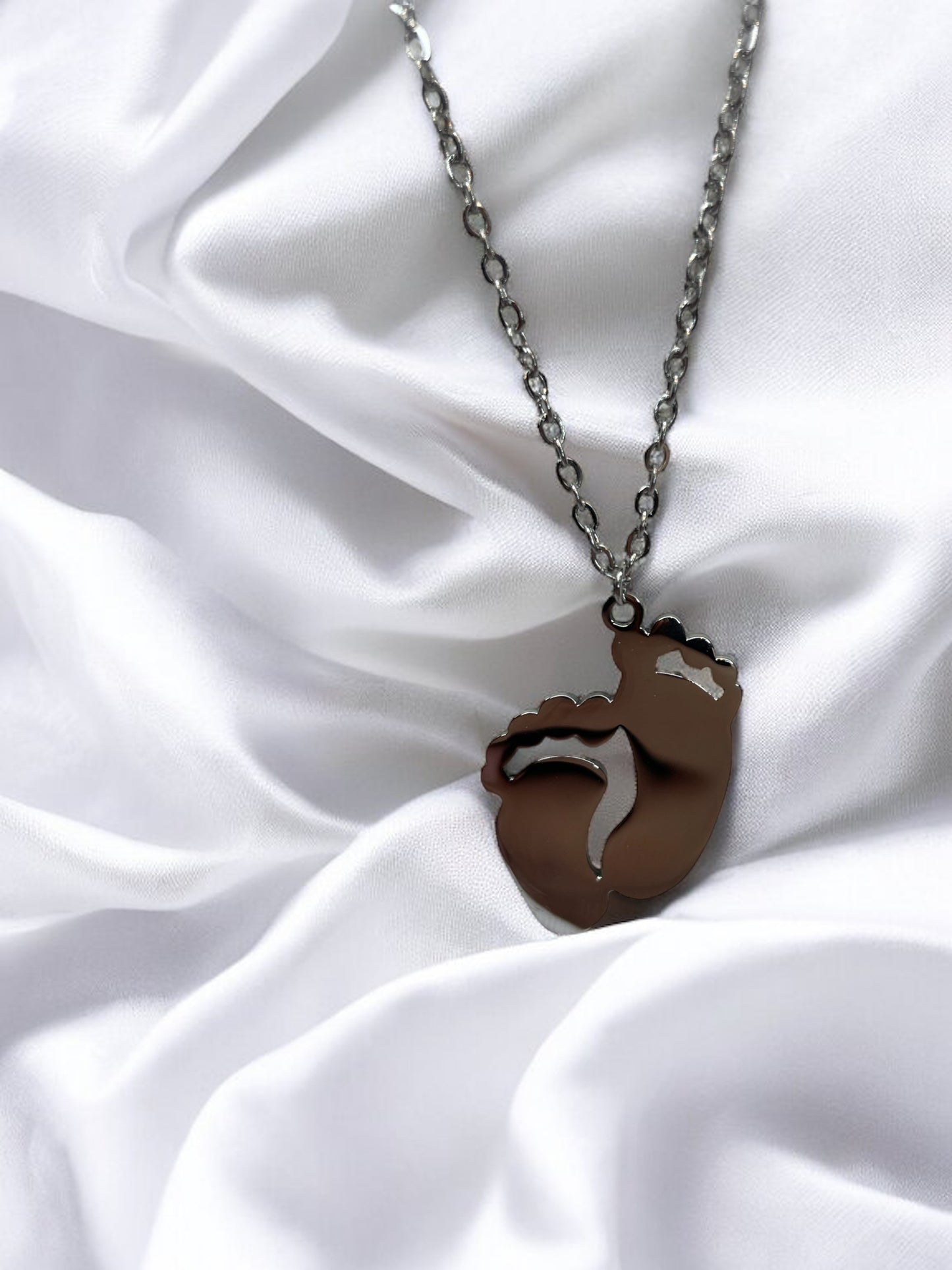 This image displays a charming necklace featuring a pendant shaped like a small child's footprint, signifying beginnings and growth. It has a polished finish with a choice between the classic sheen of stainless steel and the warm glow of gold plating. The pendant hangs gracefully on a matching chain, making it an ideal piece for everyday wear or as a sentimental gift to commemorate life's precious moments."