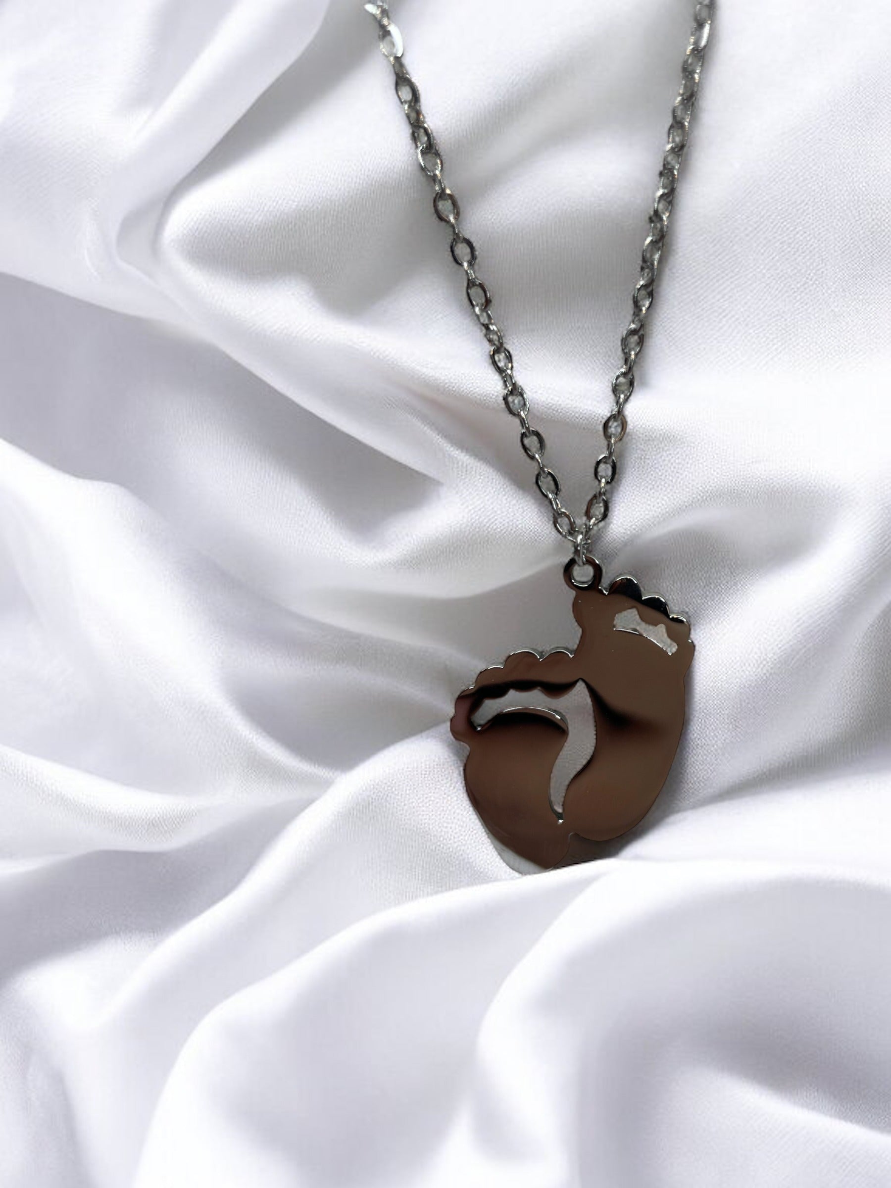 This image displays a charming necklace featuring a pendant shaped like a small child's footprint, signifying beginnings and growth. It has a polished finish with a choice between the classic sheen of stainless steel and the warm glow of gold plating. The pendant hangs gracefully on a matching chain, making it an ideal piece for everyday wear or as a sentimental gift to commemorate life's precious moments."
