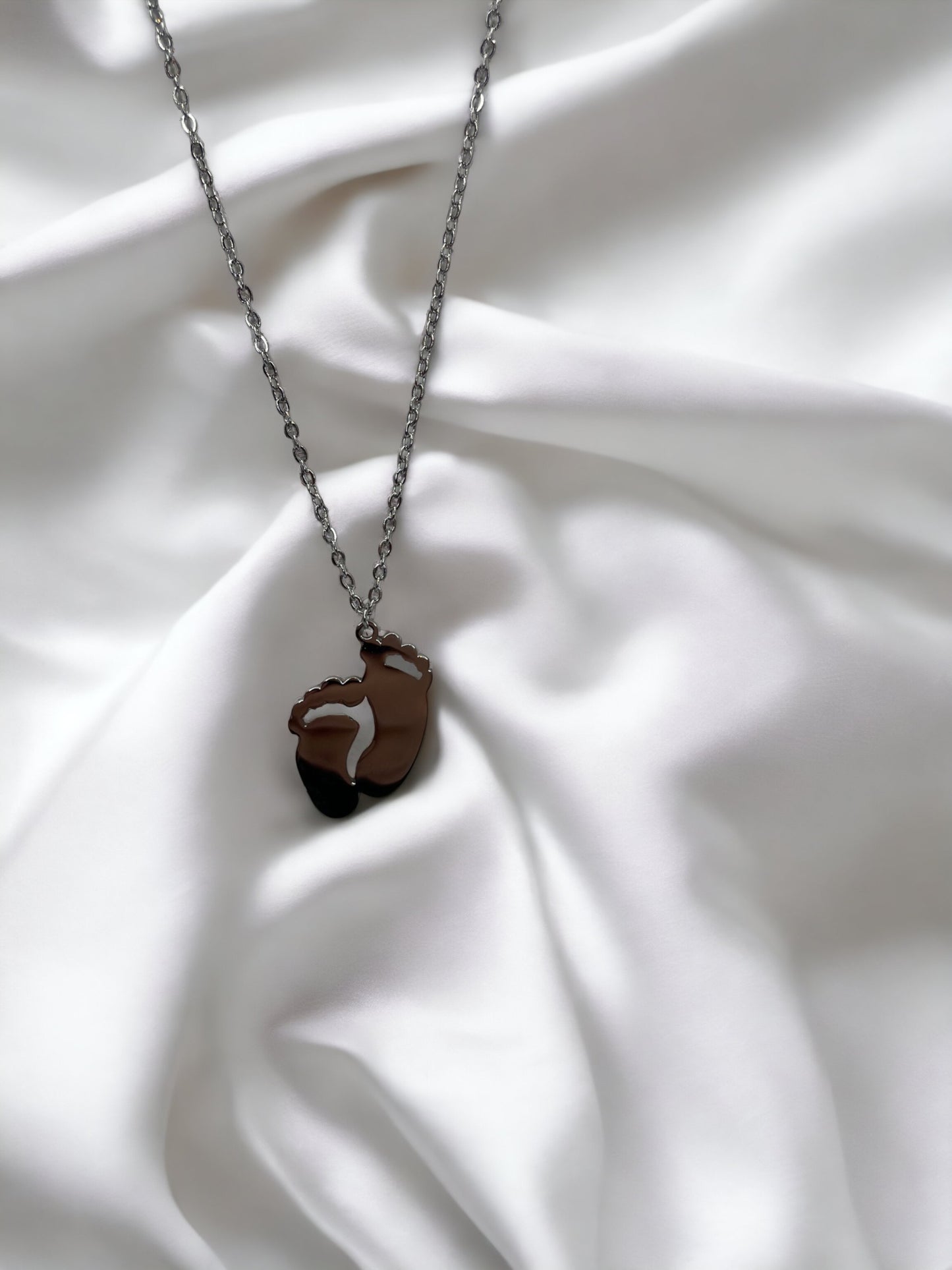 This image displays a charming necklace featuring a pendant shaped like a small child's footprint, signifying beginnings and growth. It has a polished finish with a choice between the classic sheen of stainless steel and the warm glow of gold plating. The pendant hangs gracefully on a matching chain, making it an ideal piece for everyday wear or as a sentimental gift to commemorate life's precious moments."