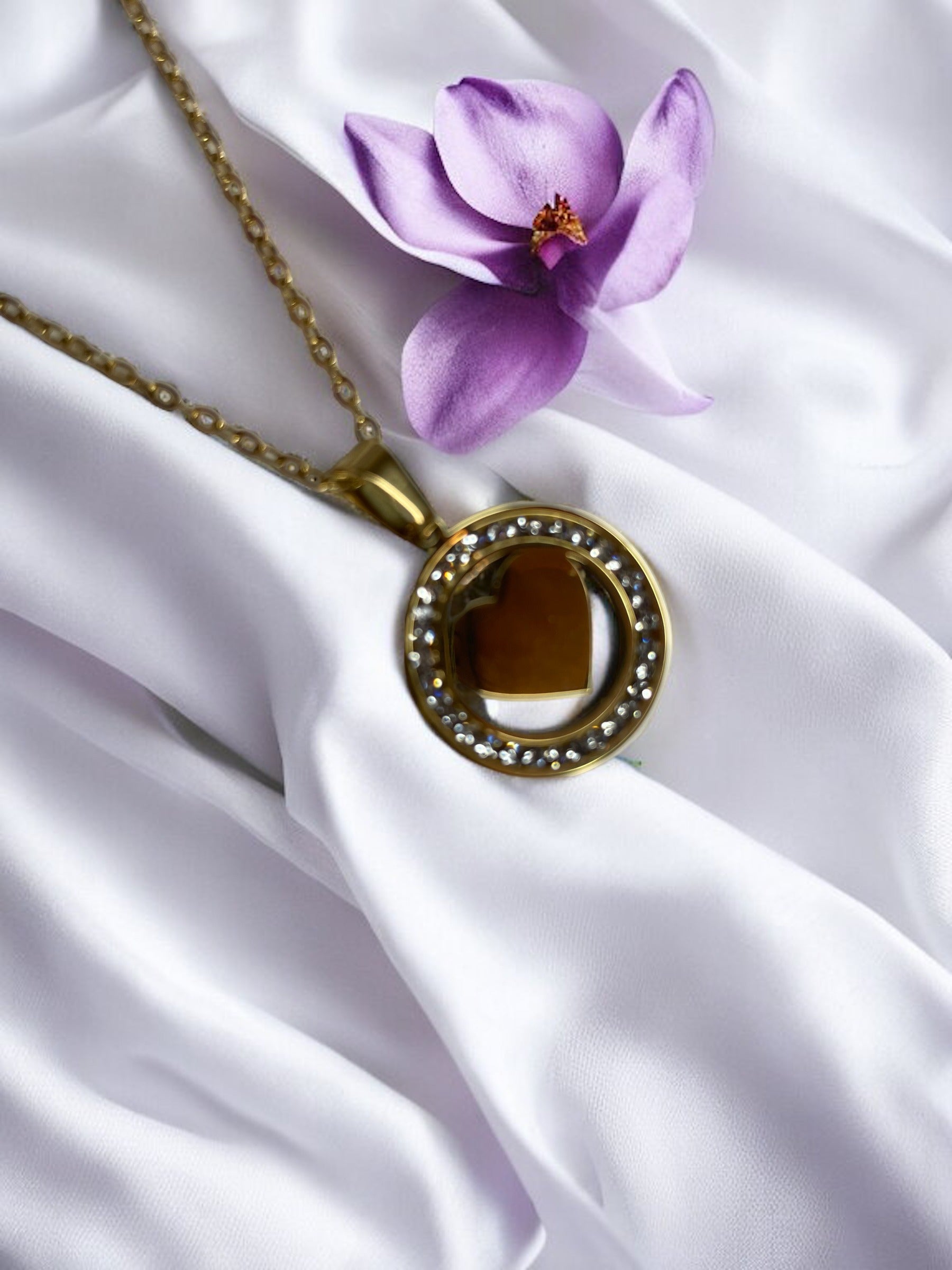 Presenting our Sparkle Heart Necklace – where elegance meets timeless charm. This necklace features a stainless steel composition with a luxurious gold finish, offering enduring beauty and resilience. At its center is a captivating heart, encased within a circle of shimmering cubic zirconia stones that catch the light with every movement. 