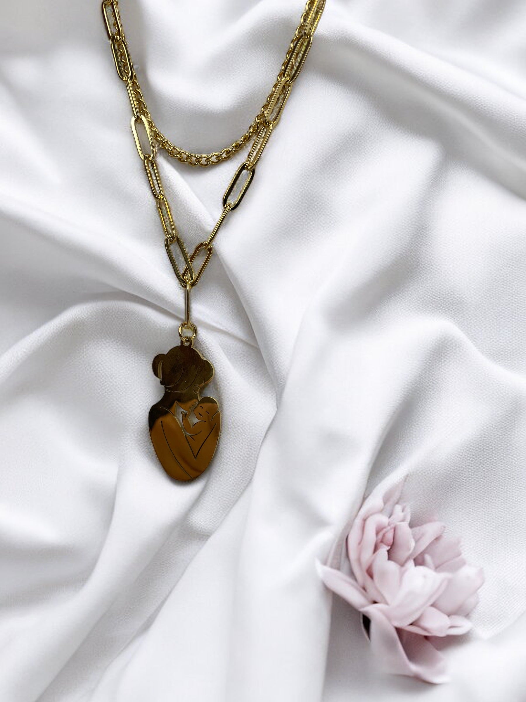 The Maternal Grace Pendant Necklace features a sophisticated design with a mother and her baby in a gentle embrace, forming an abstract heart shape within the pendant. Depending on your selection, the pendant comes in the resilient sheen of stainless steel or the timeless elegance of gold plating. The accompanying chain is tastefully designed to complement the pendant, making the necklace a graceful statement of motherly love and tenderness.