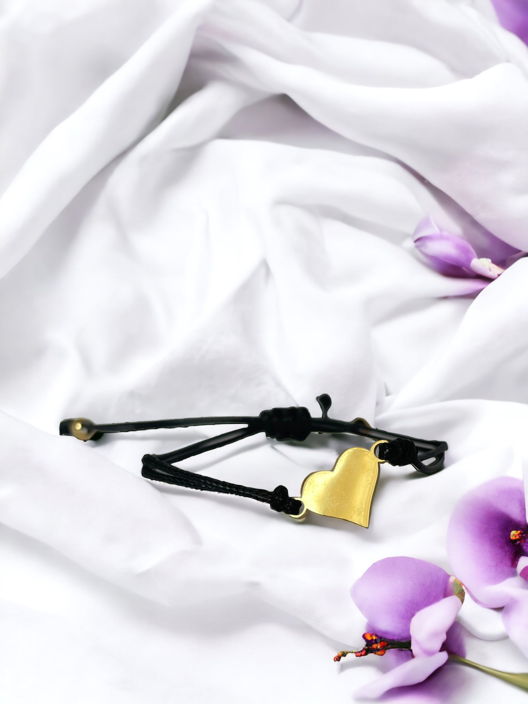 The heart has a smooth, metallic finish and is strung on a slender, black adjustable cord for a comfortable and customizable fit. It strikes a balance between casual and chic, making it suitable for a variety of occasions. The bracelet is available in two options: a classic, shiny stainless steel, or a rich, gold-plated finish, offering a choice to suit different styles and preferences. It's a piece that's designed to be both sentimental and stylish, perfect for everyday wear or as a thoughtful gift.