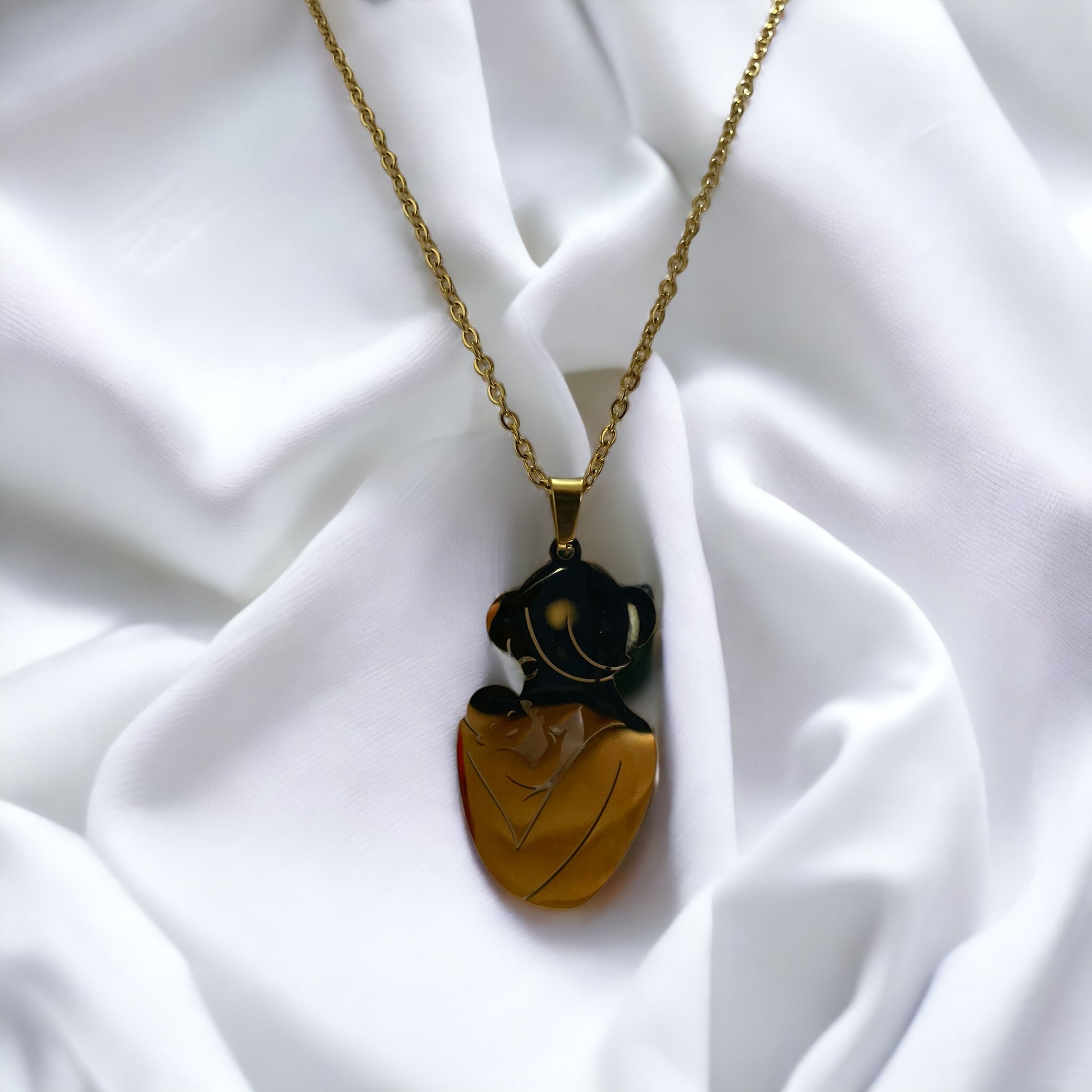  The image displays a necklace with a pendant featuring the silhouette of a mother holding her baby close. The design is simple yet evocative, capturing a moment of tenderness between parent and child. The pendant is available in two finishes: a lustrous stainless steel and a warm gold plating. It hangs from a matching chain, complementing the pendant's finish. The necklace embodies a sense of nurturing love and would make a thoughtful gift or a personal keepsake, symbolizing the bond of motherhood.