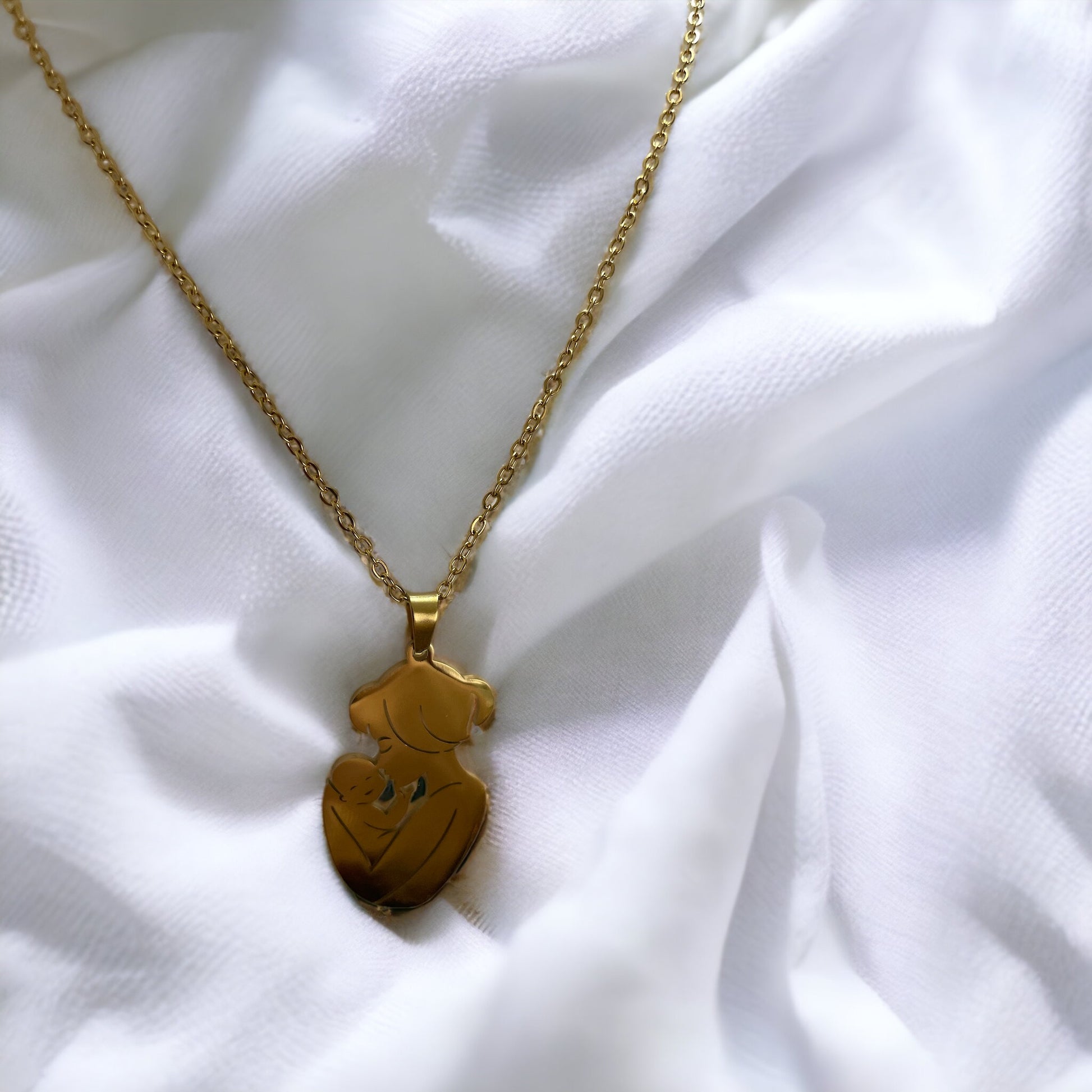  The image displays a necklace with a pendant featuring the silhouette of a mother holding her baby close. The design is simple yet evocative, capturing a moment of tenderness between parent and child. The pendant is available in two finishes: a lustrous stainless steel and a warm gold plating. It hangs from a matching chain, complementing the pendant's finish. The necklace embodies a sense of nurturing love and would make a thoughtful gift or a personal keepsake, symbolizing the bond of motherhood.