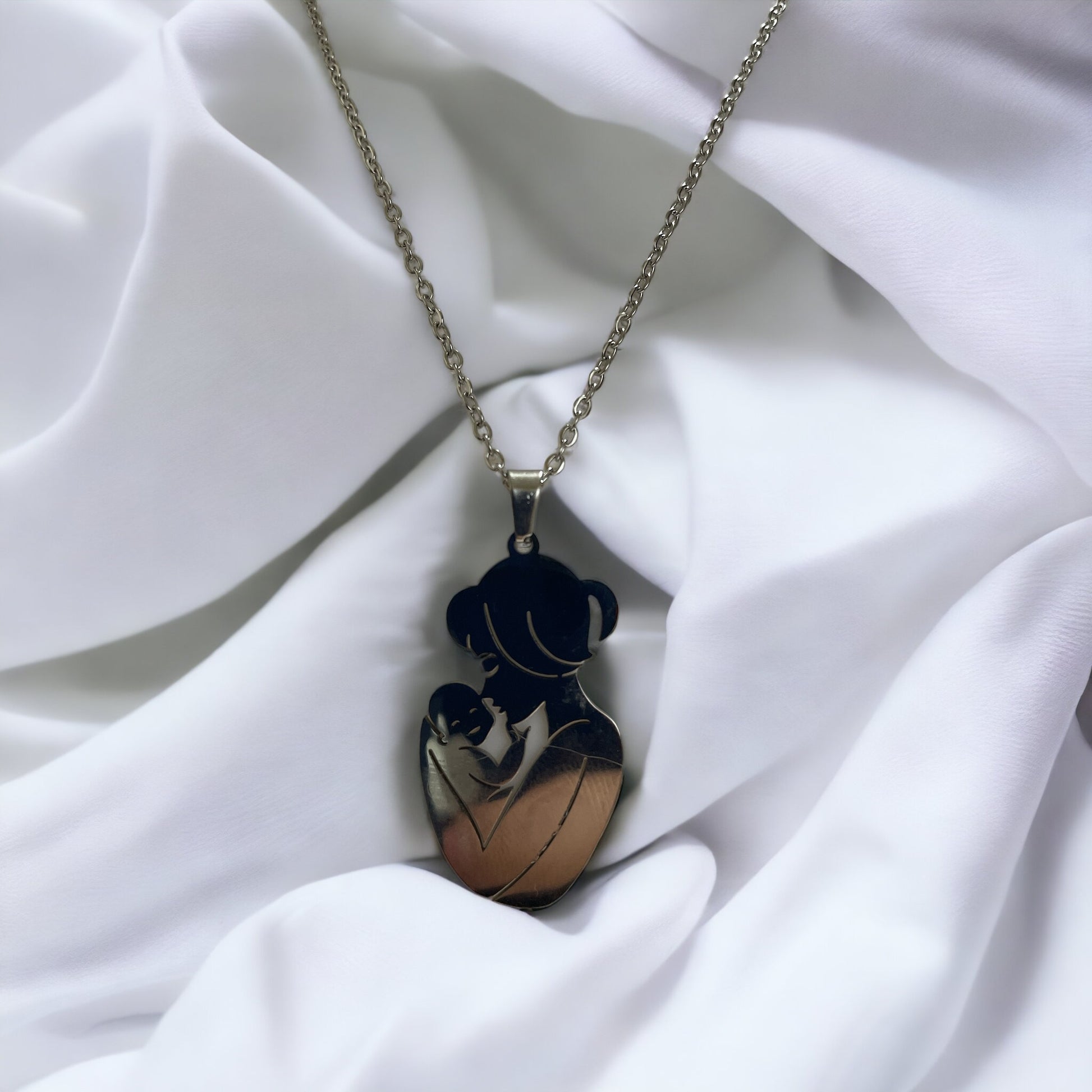  The image displays a necklace with a pendant featuring the silhouette of a mother holding her baby close. The design is simple yet evocative, capturing a moment of tenderness between parent and child. The pendant is available in two finishes: a lustrous stainless steel and a warm gold plating. It hangs from a matching chain, complementing the pendant's finish. The necklace embodies a sense of nurturing love and would make a thoughtful gift or a personal keepsake, symbolizing the bond of motherhood.