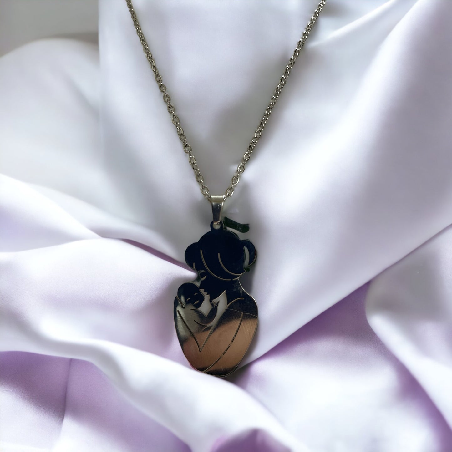  The image displays a necklace with a pendant featuring the silhouette of a mother holding her baby close. The design is simple yet evocative, capturing a moment of tenderness between parent and child. The pendant is available in two finishes: a lustrous stainless steel and a warm gold plating. It hangs from a matching chain, complementing the pendant's finish. The necklace embodies a sense of nurturing love and would make a thoughtful gift or a personal keepsake, symbolizing the bond of motherhood.