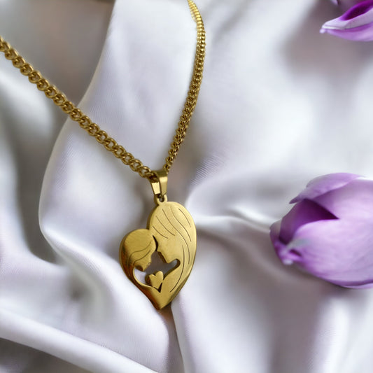 This image features the "Maternal Embrace Heart Pendant," a beautifully crafted piece with a silhouette of a mother and her child in a tender embrace, forming a heart shape. The pendant has a rich, golden hue, suggesting it is available in gold plating, with an option for stainless steel as well. It is draped over a delicate, magnolia petal, surrounded by soft, pastel flowers, enhancing the pendant's elegance and the sentiment it represents.