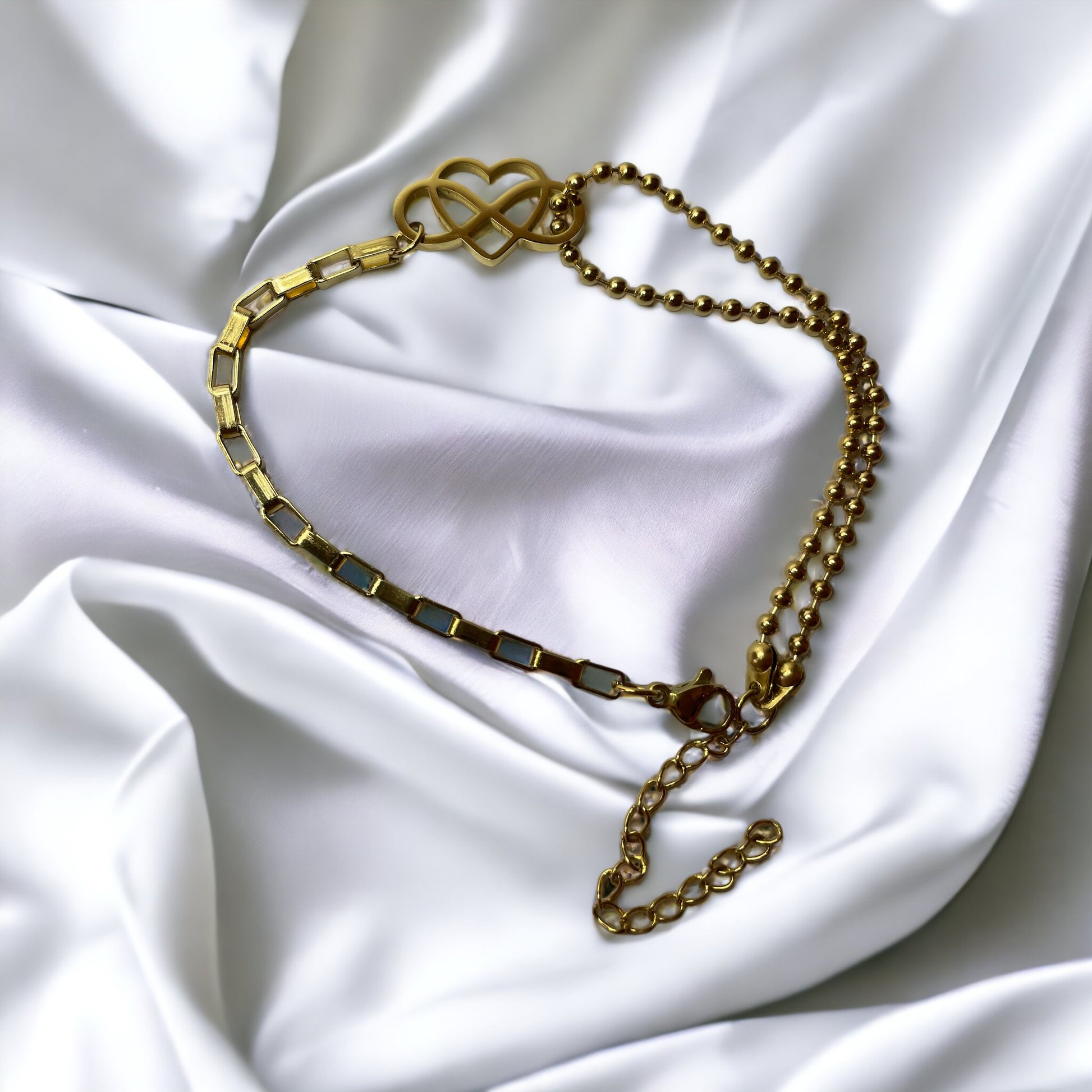 This "Eternal Embrace Bracelet" features a striking geometric heart charm that artistically intersects, symbolizing infinity and enduring love. The charm is tastefully attached to a mixed chain design composed of both a smooth, polished link chain and a rounded bead chain, adding a playful contrast to the bracelet. It is available in two finishes: a shiny stainless steel for a sleek look and a rich gold plating for a touch of warmth. 