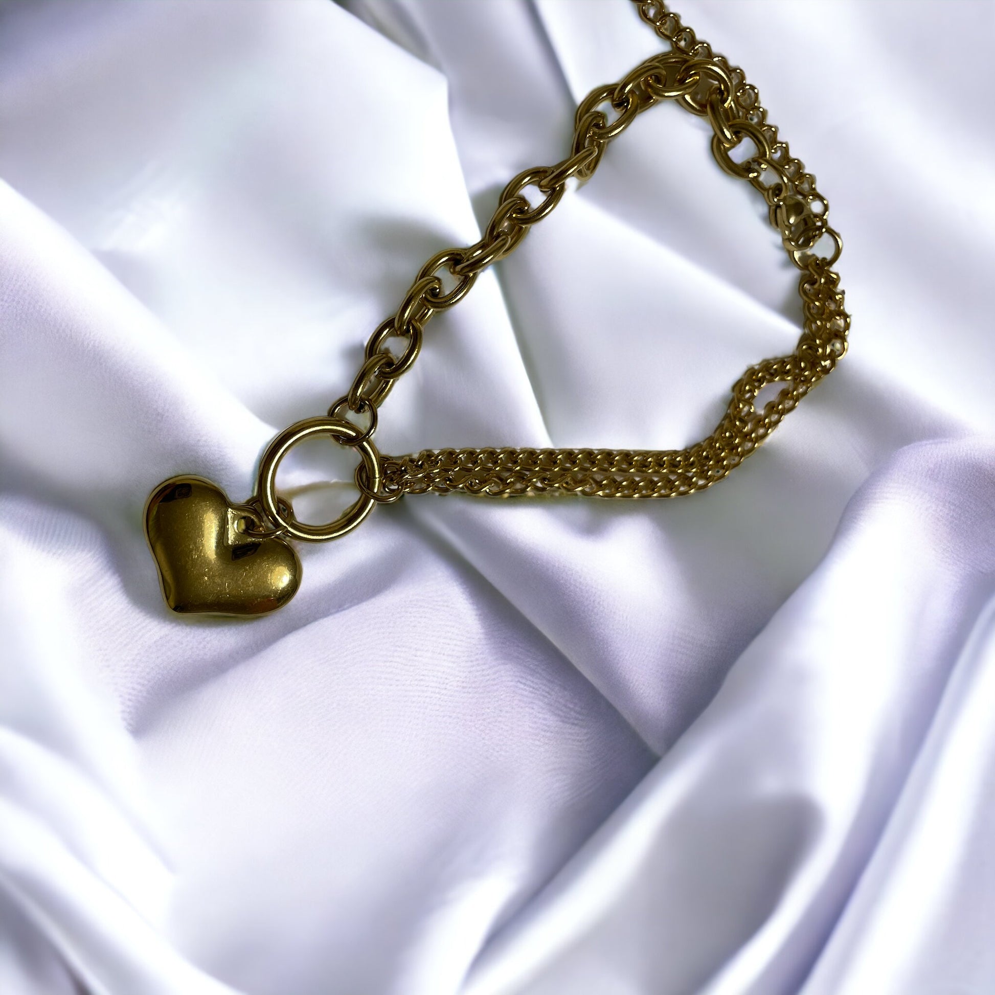 The heart charm adds a romantic and personal touch, making it a standout accessory that symbolizes love and warmth. This bracelet is also available in a stainless steel finish, offering a sleek and modern alternative to the classic gold, ensuring durability and a lasting sheen. It's a versatile piece that can be worn alone for a subtle statement or layered with other bracelets for a more personalized look.
