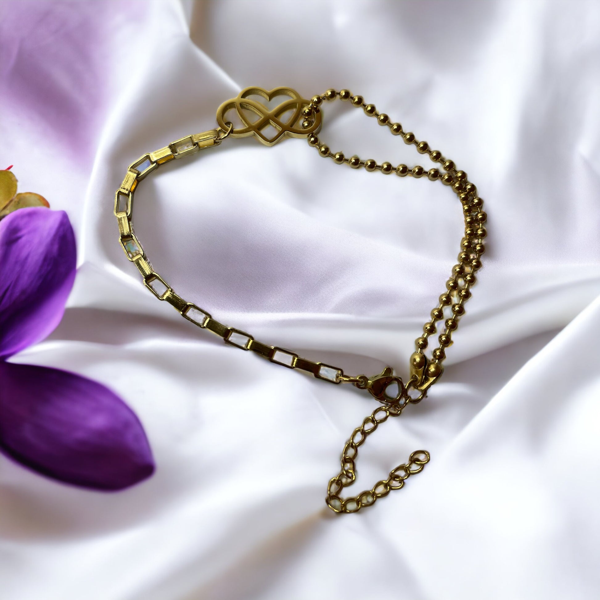 This "Eternal Embrace Bracelet" features a striking geometric heart charm that artistically intersects, symbolizing infinity and enduring love. The charm is tastefully attached to a mixed chain design composed of both a smooth, polished link chain and a rounded bead chain, adding a playful contrast to the bracelet. It is available in two finishes: a shiny stainless steel for a sleek look and a rich gold plating for a touch of warmth. 