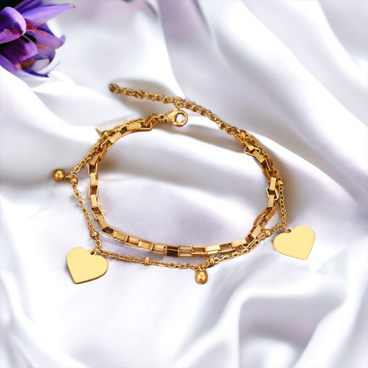 This image displays a stylish, two-layer bracelet with a polished heart charm, representing love and connection. Available in stainless steel with options for gold plating or silver finish, the bracelet combines a box chain with a beaded chain, creating a simple yet elegant accessory suitable for everyday wear or special occasions.