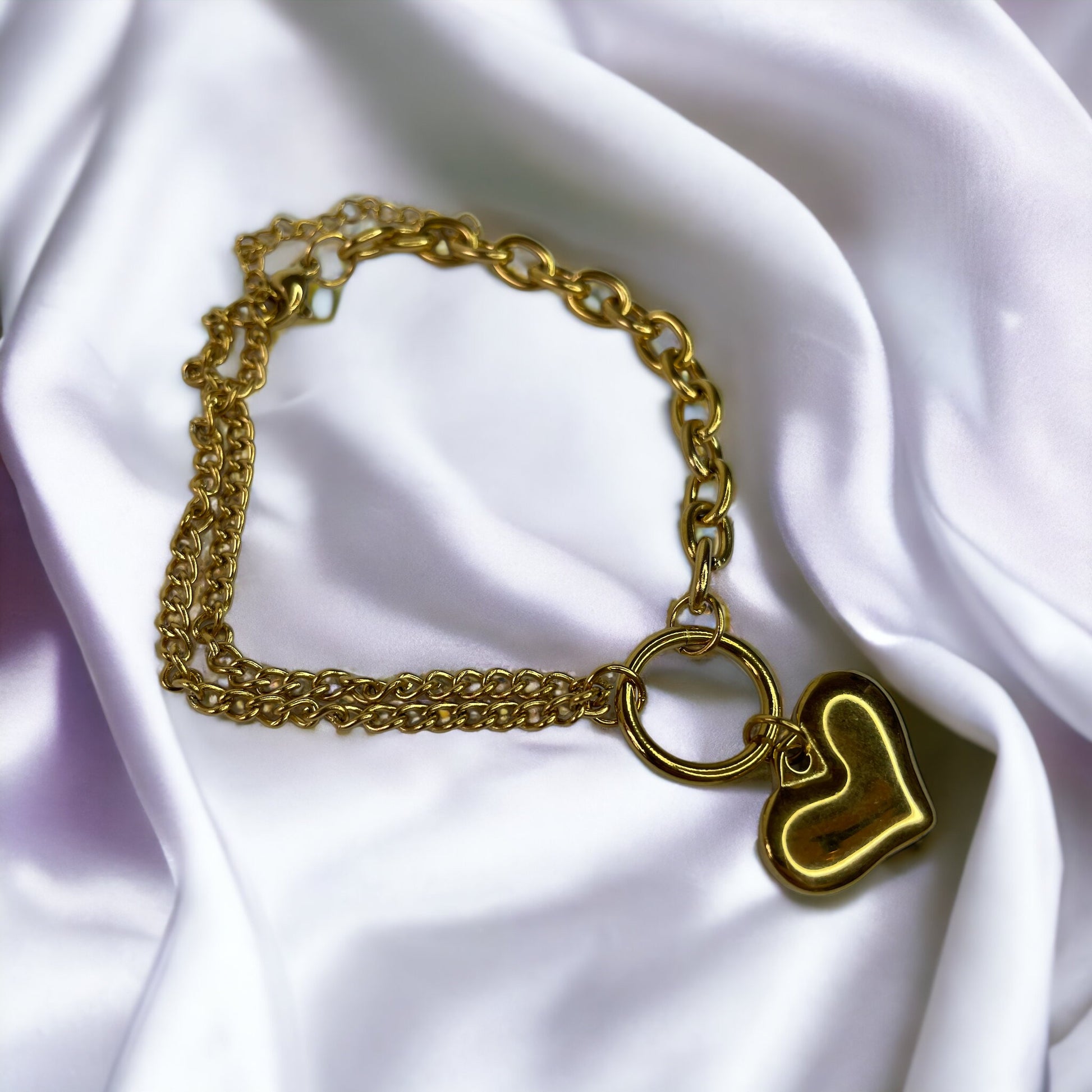 The heart charm adds a romantic and personal touch, making it a standout accessory that symbolizes love and warmth. This bracelet is also available in a stainless steel finish, offering a sleek and modern alternative to the classic gold, ensuring durability and a lasting sheen. It's a versatile piece that can be worn alone for a subtle statement or layered with other bracelets for a more personalized look.