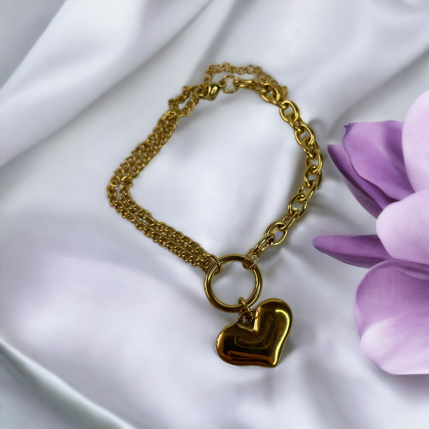 The heart charm adds a romantic and personal touch, making it a standout accessory that symbolizes love and warmth. This bracelet is also available in a stainless steel finish, offering a sleek and modern alternative to the classic gold, ensuring durability and a lasting sheen. It's a versatile piece that can be worn alone for a subtle statement or layered with other bracelets for a more personalized look.
