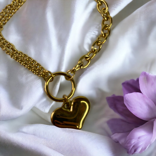The heart charm adds a romantic and personal touch, making it a standout accessory that symbolizes love and warmth. This bracelet is also available in a stainless steel finish, offering a sleek and modern alternative to the classic gold, ensuring durability and a lasting sheen. It's a versatile piece that can be worn alone for a subtle statement or layered with other bracelets for a more personalized look.