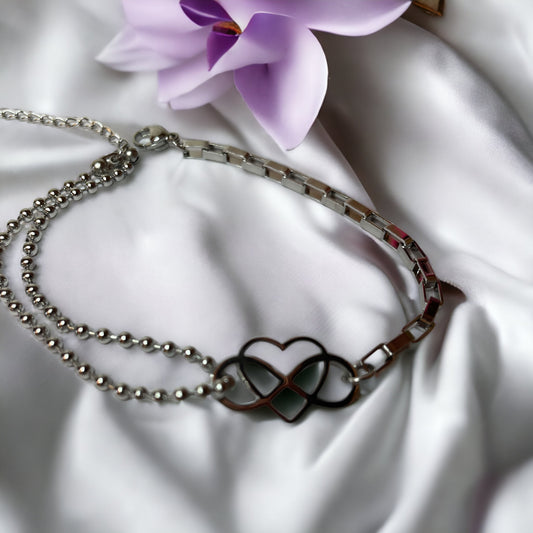This "Eternal Embrace Bracelet" features a striking geometric heart charm that artistically intersects, symbolizing infinity and enduring love. The charm is tastefully attached to a mixed chain design composed of both a smooth, polished link chain and a rounded bead chain, adding a playful contrast to the bracelet. It is available in two finishes: a shiny stainless steel for a sleek look and a rich gold plating for a touch of warmth. 
