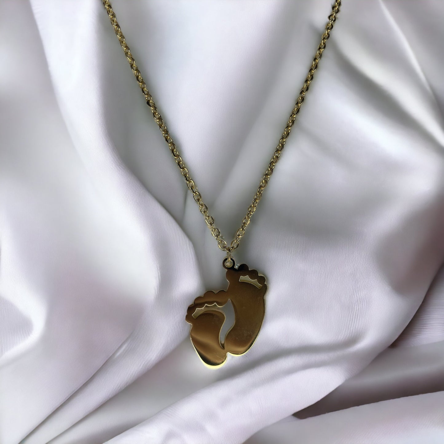 This image displays a charming necklace featuring a pendant shaped like a small child's footprint, signifying beginnings and growth. It has a polished finish with a choice between the classic sheen of stainless steel and the warm glow of gold plating. The pendant hangs gracefully on a matching chain, making it an ideal piece for everyday wear or as a sentimental gift to commemorate life's precious moments."