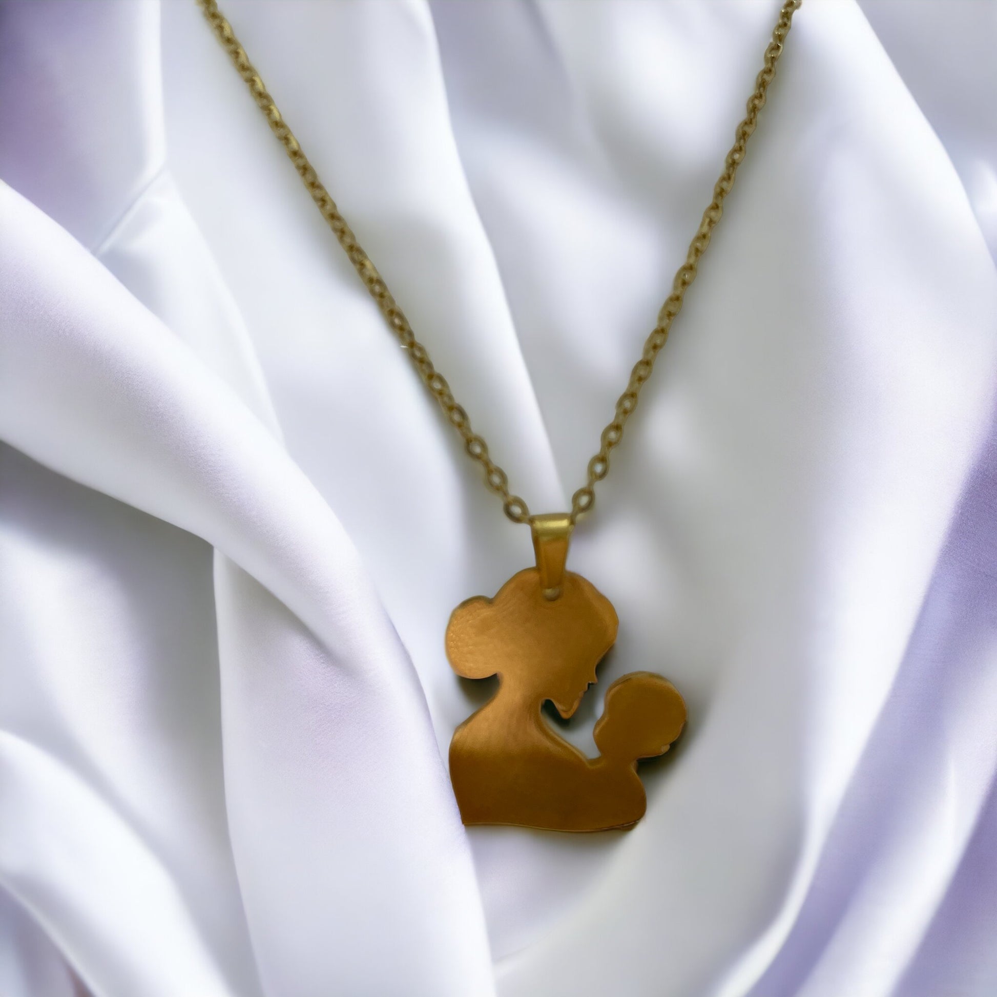 You are viewing a necklace with a pendant that artistically represents a mother holding her child. The pendant's design is abstract, with smooth, flowing lines that outline the figures, merging into a single form. The pendant is golden in color, hinting at a gold-plated material, although it is also available in stainless steel. It hangs on a matching golden chain that complements the pendant's warm tones. This piece is designed to embody the warmth and love of the maternal bond.