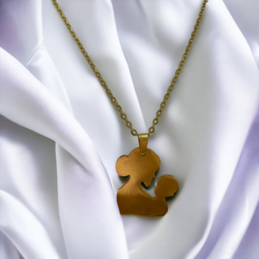 You are viewing a necklace with a pendant that artistically represents a mother holding her child. The pendant's design is abstract, with smooth, flowing lines that outline the figures, merging into a single form. The pendant is golden in color, hinting at a gold-plated material, although it is also available in stainless steel. It hangs on a matching golden chain that complements the pendant's warm tones. This piece is designed to embody the warmth and love of the maternal bond.