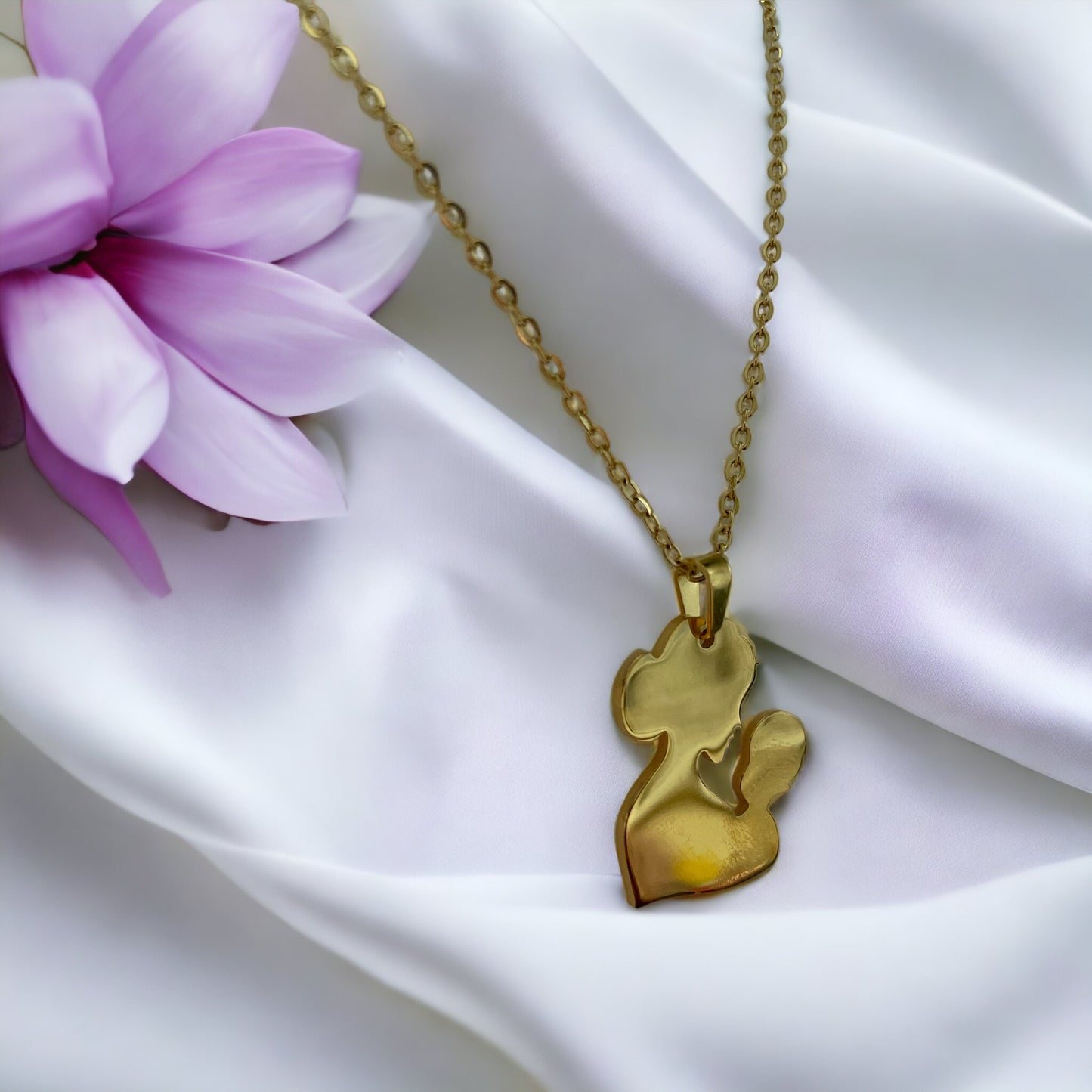You are viewing a necklace with a pendant that artistically represents a mother holding her child. The pendant's design is abstract, with smooth, flowing lines that outline the figures, merging into a single form. The pendant is golden in color, hinting at a gold-plated material, although it is also available in stainless steel. It hangs on a matching golden chain that complements the pendant's warm tones. This piece is designed to embody the warmth and love of the maternal bond.
