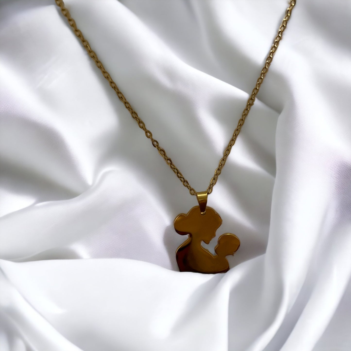 You are viewing a necklace with a pendant that artistically represents a mother holding her child. The pendant's design is abstract, with smooth, flowing lines that outline the figures, merging into a single form. The pendant is golden in color, hinting at a gold-plated material, although it is also available in stainless steel. It hangs on a matching golden chain that complements the pendant's warm tones. This piece is designed to embody the warmth and love of the maternal bond.