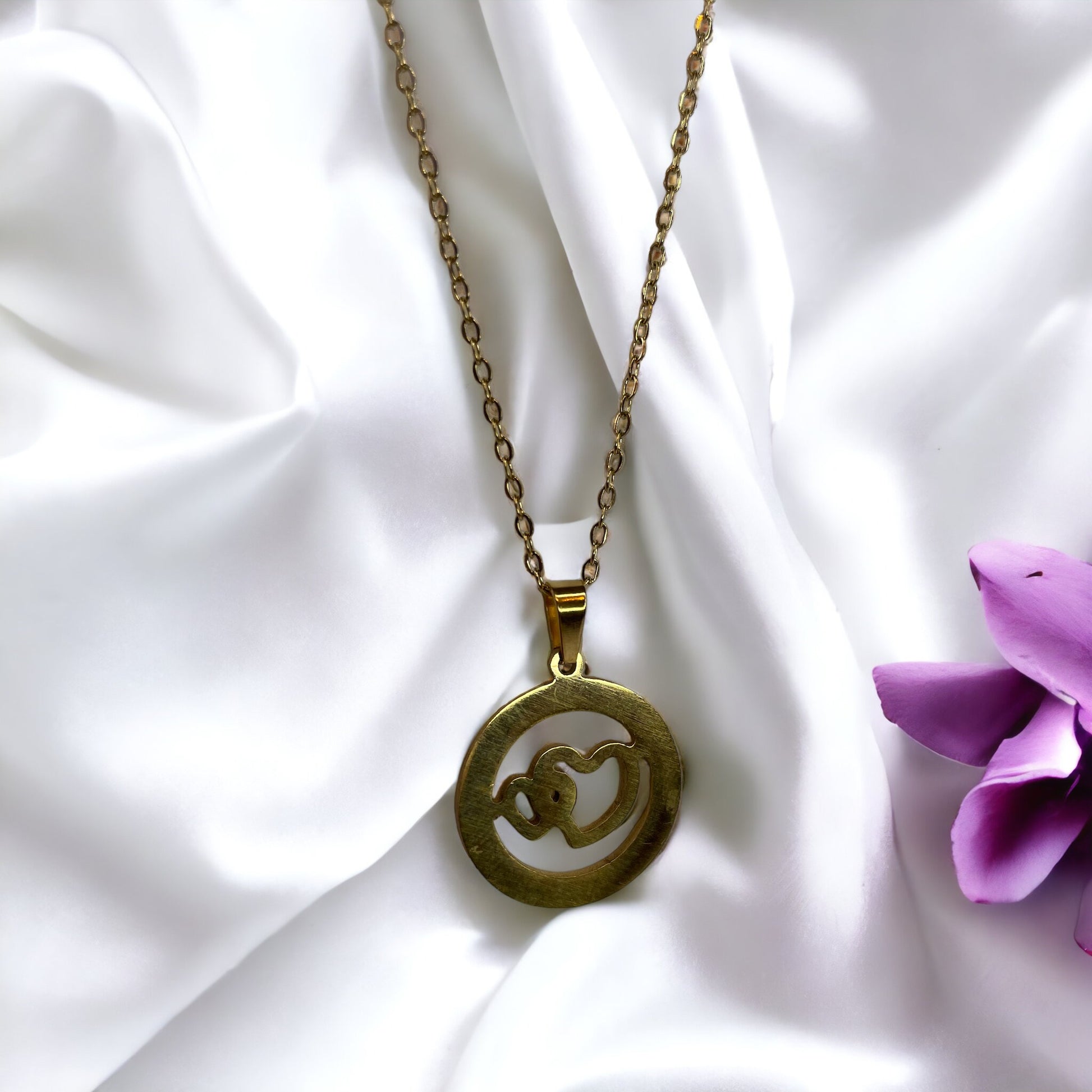 The Infinite Embrace Necklace features a round, disc-shaped pendant in a golden hue. Within it, two stylized figures come together in an embrace, forming an infinite loop that symbolizes continuity and eternal connection. This design is both simple and profound, offering a timeless message of love and unity. It's available in options of stainless steel or gold-plated finishes, ensuring durability along with elegance."