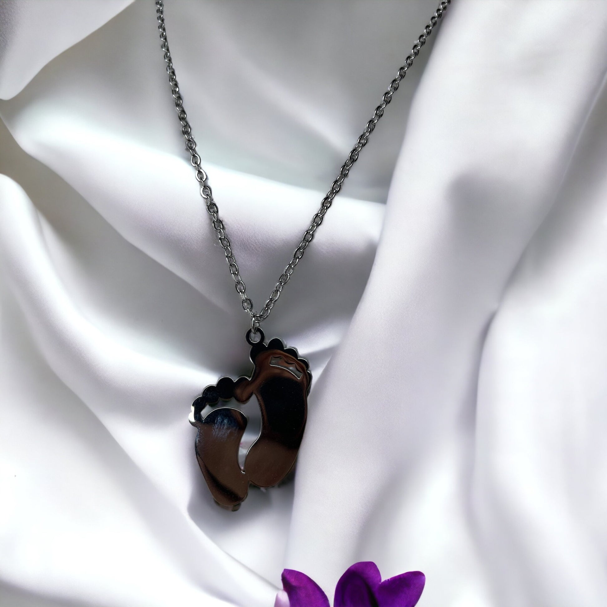This image displays a charming necklace featuring a pendant shaped like a small child's footprint, signifying beginnings and growth. It has a polished finish with a choice between the classic sheen of stainless steel and the warm glow of gold plating. The pendant hangs gracefully on a matching chain, making it an ideal piece for everyday wear or as a sentimental gift to commemorate life's precious moments."